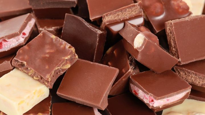 St&uuml;cke von Schokolade liegen gestapelt, teils mit N&uuml;ssen und Fruchtf&uuml;llungen, in einer bunten Mischung angeordnet.