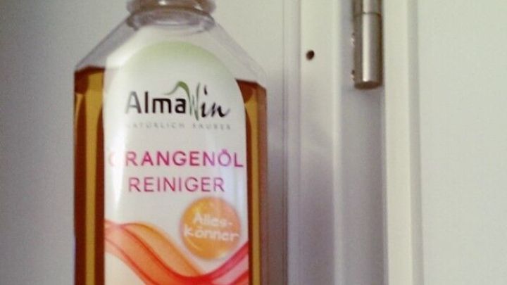 Eine Flasche Orangen&ouml;lreiniger wird an einer T&uuml;rdichtung gehalten, die gereinigt werden soll, in einem hellen Raum.