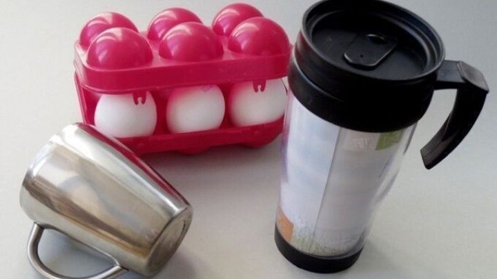 Ein wiederverwendbarer Becher steht neben einem Eierkarton, der acht Eier enth&auml;lt, auf einer hellen Tischoberfl&auml;che.