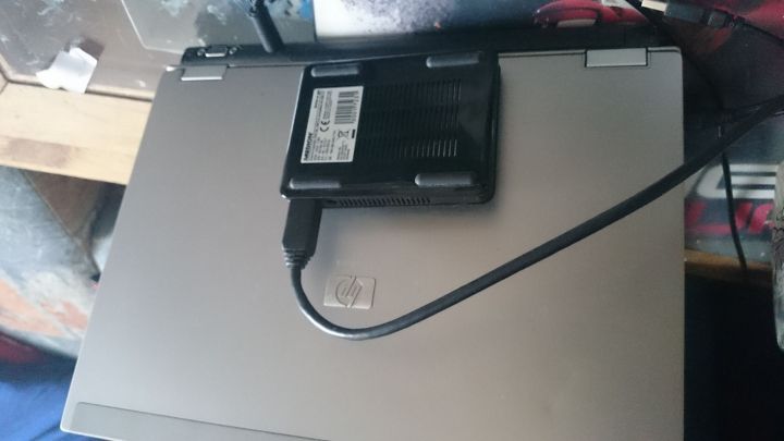 Eine externe Festplatte ist &uuml;ber ein Kabel mit einem Laptop verbunden und steht auf der Laptop-Oberfl&auml;che, in einer chaotischen Umgebung.