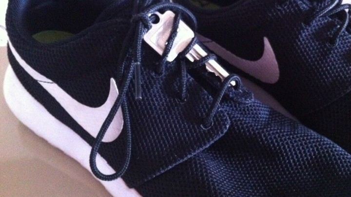 Schwarze Jogging-Schuhe liegen auf einem Tisch, w&auml;hrend der Schn&uuml;rsenkel locker auf dem Schuhblatt h&auml;ngt.