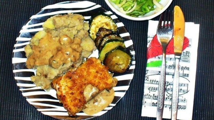 Knuspriges Fischfilet liegt auf einem gestreiften Teller, begleitet von Gem&uuml;se und frischem Salat in einer Sch&uuml;ssel.