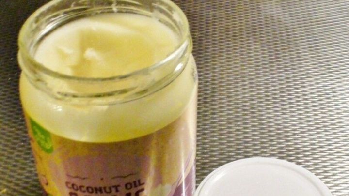 Ein Glas Kokosfett steht offen auf einem metallischen Untergrund, bereit zur Verwendung in der K&uuml;che, um Gerichte zu verfeinern.