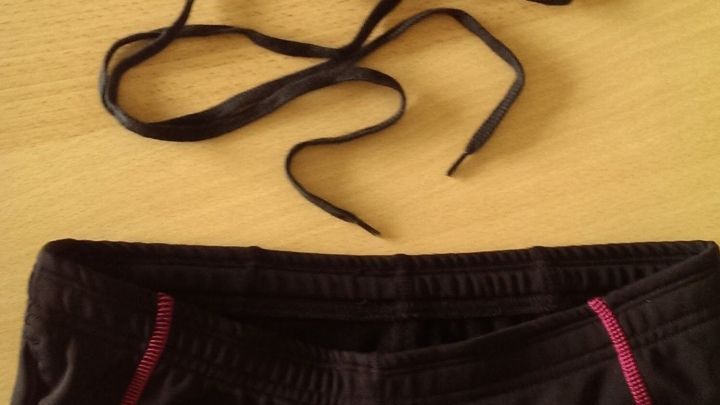 Eine Hose mit losem Zugband liegt auf einem Tisch, w&auml;hrend Schn&uuml;rsenkel daneben liegen, bereit zum Ersetzen.