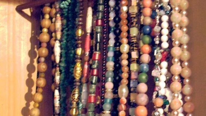 Halsketten h&auml;ngen ordentlich an einem Hosenb&uuml;gel, farbenfroh und vielf&auml;ltig, in einem Holzschrank aufgeh&auml;ngt.