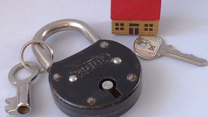 Ein gro&szlig;er Vorh&auml;ngeschloss liegt neben einem kleinen Haus und einem Schl&uuml;ssel, der Sicherheit und den Schl&uuml;ssel verstecken symbolisiert.