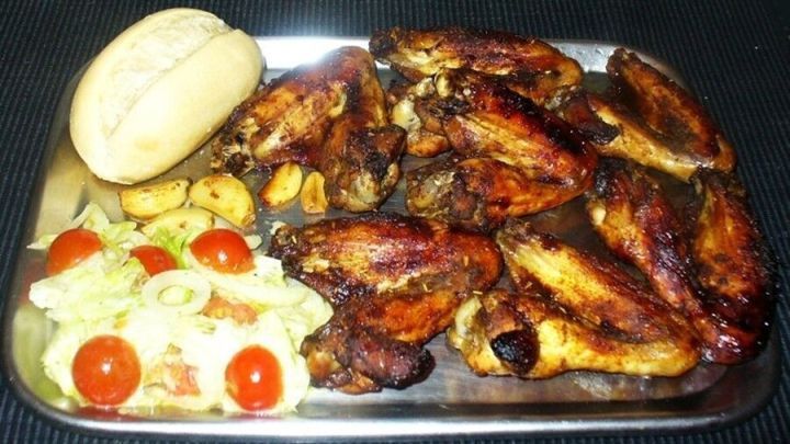 Saftige, knusprige H&auml;hnchenfl&uuml;gel liegen auf einem Tablett, umgeben von frischem Salat und einem Br&ouml;tchen.