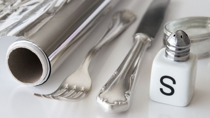 Ein gl&auml;nzendes Silberbesteck liegt zusammen mit einer Serviette und einem Salzstreuer auf einem wei&szlig;en Tisch, bereit zur Nutzung.