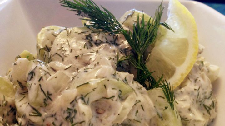 Warmer Gurkensalat mit Dill und Sauerrahm wird appetitlich in einer Sch&uuml;ssel angerichtet, mit Zitronenscheiben und frischem Dill garniert.