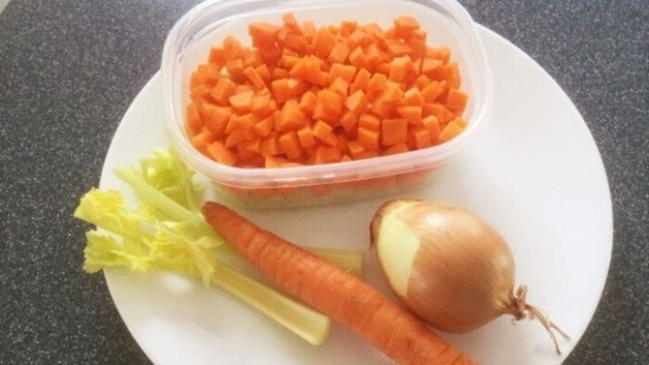 Auf einem Teller liegen gew&uuml;rfelte Karotten in einer Sch&uuml;ssel, daneben eine Karotte, eine Zwiebel und ein St&uuml;ck Sellerie, bereit f&uuml;r Eintopf.