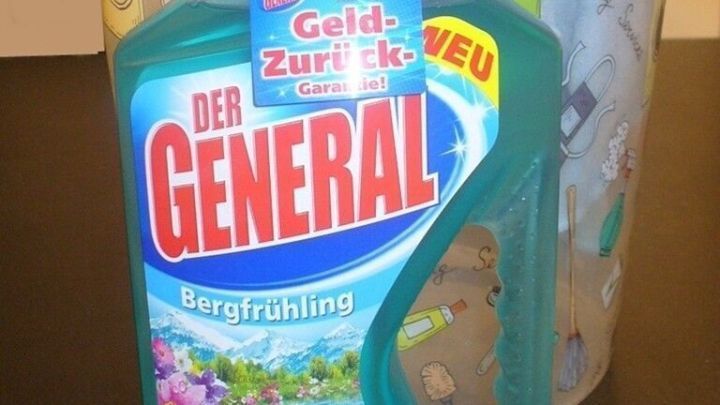 Flasche mit &bdquo;Der General&ldquo; Sp&uuml;lmittel steht auf Tisch, umgeben von einem bunten M&uuml;lleimer und einem Handtuch.