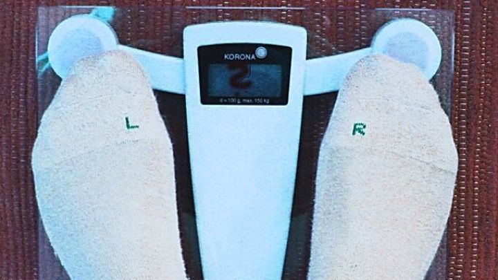 Eine Personenwaage zeigt eine Zahl an, w&auml;hrend F&uuml;&szlig;e mit Socken darauf stehen, im Kontext von Gesundheit und Alkohol am Abend.