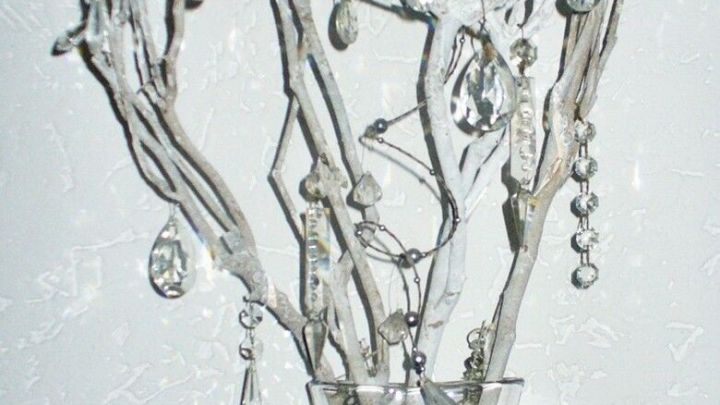 &Auml;ste mit glitzernden Anh&auml;ngern stehen in einer klaren Vase, umgeben von dekorativem glitzerndem Material und Gl&auml;sern.