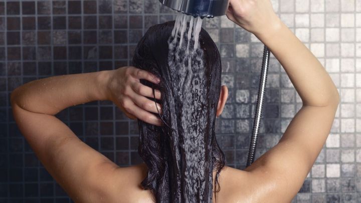 Eine Person w&auml;scht sich im Duschraum die Haare mit Shampoo unter einem Wasserstrahl, um Shampoo zu sparen.
