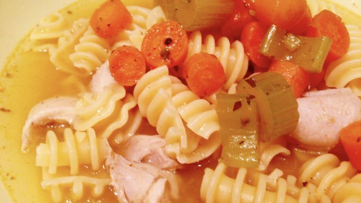 Eine Nudelsuppe mit H&auml;hnchenfleisch, frischen Karotten und Sellerie in einer klaren Br&uuml;he in einer Sch&uuml;ssel serviert.