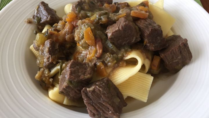 Rindergulasch liegt auf Bandnudeln auf einem Teller. Das Gericht ist mit einer dunklen So&szlig;e und Gem&uuml;se garniert.