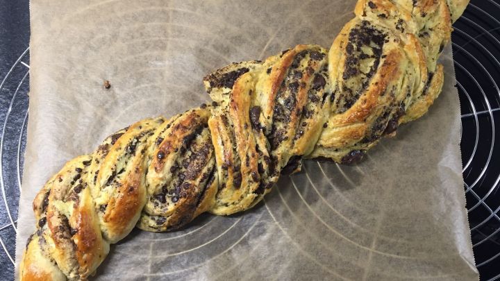 Ein frisch gebackener Schokoladenzopf liegt auf Backpapier und pr&auml;sentiert seine goldenen, schokoladigen Str&auml;nge.