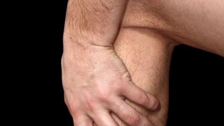 Ein Mann h&auml;lt sich am Schienbein, offenbar aufgrund von Juckreiz oder Unbehagen; der Hintergrund ist schwarz.