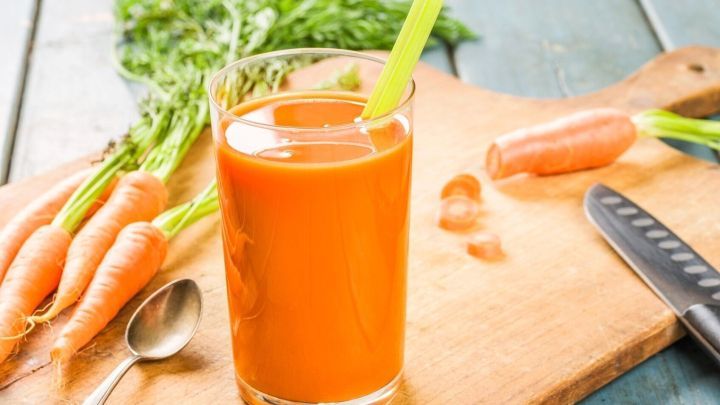 Ein Glas frischer Karottensaft steht auf einem Holzbrett, umgeben von Karotten und einem K&uuml;chenmesser, ideal f&uuml;r gesundes Fasten.