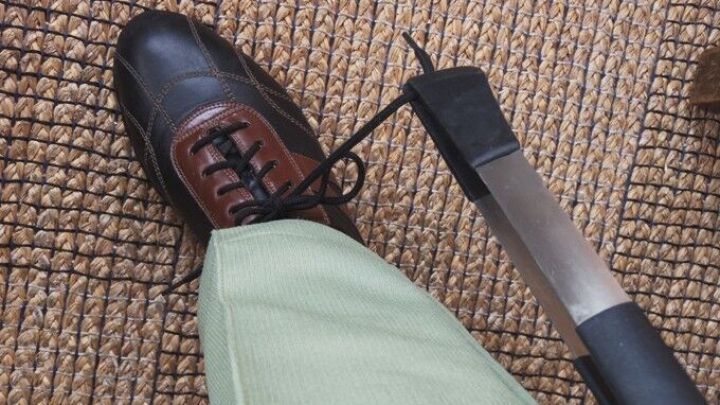 Ein Schuh liegt auf einem Teppich, w&auml;hrend ein Schn&uuml;rsenkel gel&ouml;st wird, was R&uuml;ckenprobleme ansprechen k&ouml;nnte.