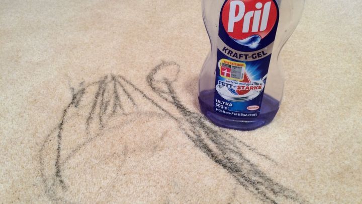 Auf einem hellen Teppich steht eine Flasche Pril, w&auml;hrend sich neben ihr bunte Wachsmalstiftfarbe befindet, die entfernt wird.