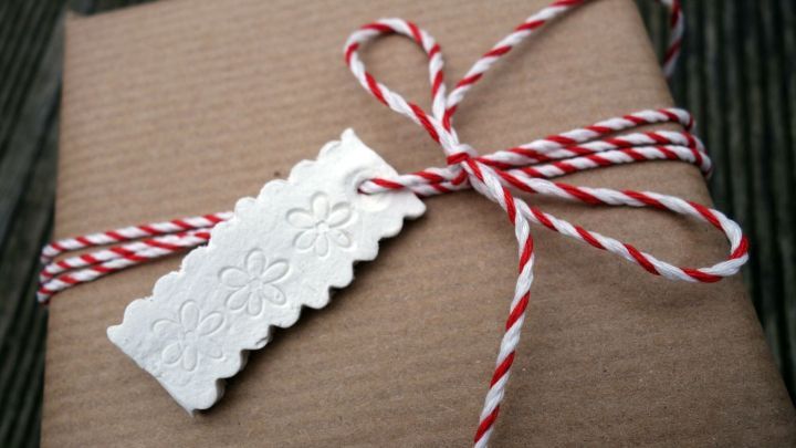 Ein Geschenkanh&auml;nger aus Modelliermasse h&auml;ngt an einem braunen Paket, das mit Rot-Wei&szlig;em Band gebunden ist.