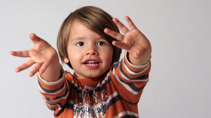 Ein fr&ouml;hliches Kind mit ausgebreiteten H&auml;nden spielt und zeigt langsam Fingerspiele vor neutralem Hintergrund.