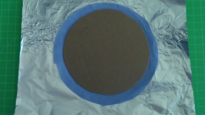 Ein runder Stoffkreis liegt auf Aluminiumfolie, w&auml;hrend er auf einer gr&uuml;nen Unterlage f&uuml;r ein kreatives Projekt vorbereitet wird.