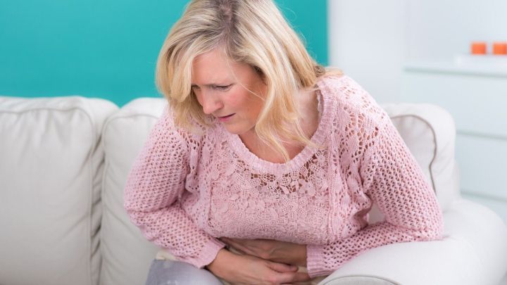 Eine Frau sitzt auf einem Sofa und h&auml;lt sich den Bauch, offensichtlich unwohl, was auf Verstopfung hinweisen k&ouml;nnte.