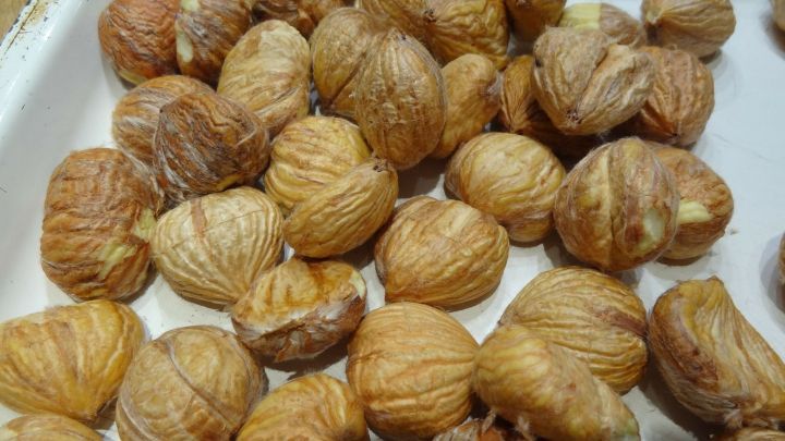 Edelkastanien liegen ungeordnet auf einem wei&szlig;en Tablett, bereit zum Konservieren oder Verzehr.