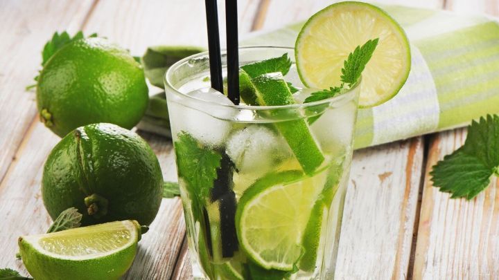 Ein erfrischender Cocktail ohne Alkohol mit Limetten und Minze steht auf einem Holztisch, umgeben von frischen Limetten.
