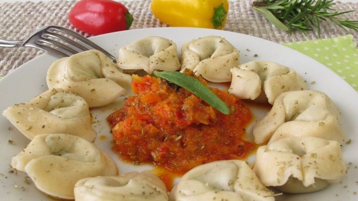 Dampfnudeln liegen auf einem Teller und sind mit milder Paprikaso&szlig;e umgeben, dekoriert mit frischem Gem&uuml;se und Kr&auml;utern.