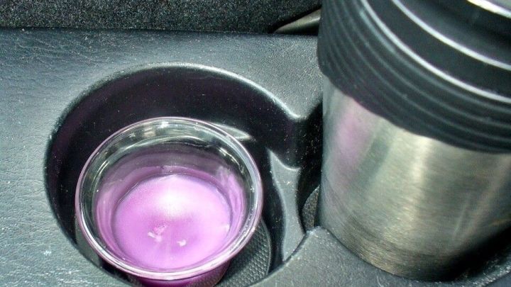 Ein kleiner Glaskelch mit lila Duft steht neben einem Edelstahlbecher in der Ablage eines Autos.