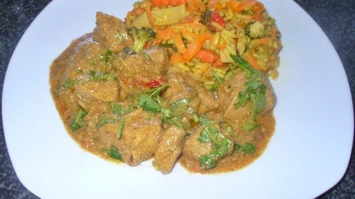 Zartes Kokos-Erdnussh&auml;hnchenfilet liegt in einer cremigen Sauce neben einem bunten Gem&uuml;semix auf einem wei&szlig;en Teller.