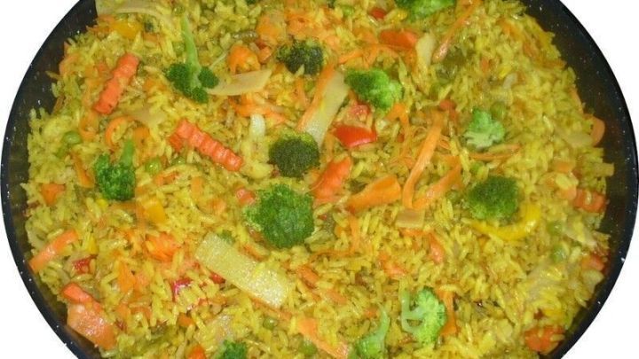 Bunter Gem&uuml;sebratreis liegt in einer gro&szlig;en Pfanne, gemischt mit buntem Gem&uuml;se und goldgelben Reis.