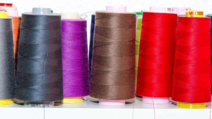 Dutzende Spulen mit Overlockgarn in verschiedenen Farben stehen nebeneinander auf einem Tisch, bereit zum sparsamen Einsatz.