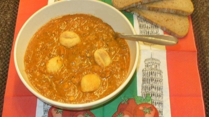 In einer wei&szlig;en Sch&uuml;ssel wird eine cremige Tomaten-K&auml;sesuppe mit Gnocchi serviert, umgeben von frischem Brot.