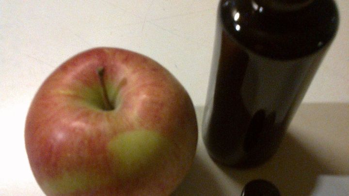 Ein roter Apfel liegt neben einer braunen Spr&uuml;hflasche, die zur Bespr&uuml;hung mit Zitronensaft verwendet wird.