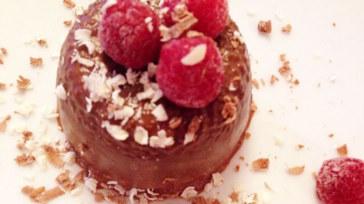 Ein schokoladiger Chia-Samen-Pudding oder Eis, garniert mit Himbeeren und Kokosraspeln, auf einem wei&szlig;en Teller angerichtet.