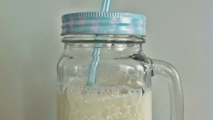 Ein Glas Nussmilch steht auf einem gr&uuml;nen Tuch und hat einen Strohhalm, bereit zum Trinken in einer hellen Umgebung.