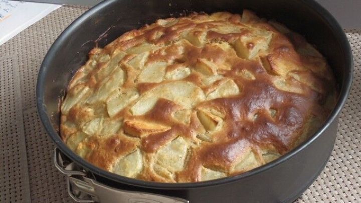 Ein frisch gebackener Birnenkuchen in einer Springform liegt auf einer Tischdecke aus gewebtem Material, leicht goldbraun.