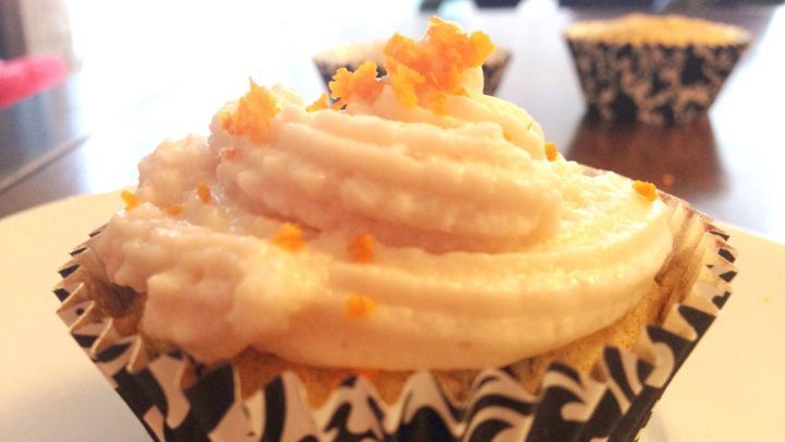 Cranberry-Orange-Cupcakes stehen auf einem wei&szlig;en Teller, mit einer cremigen, dekorativen Glasur und buntem Topping.