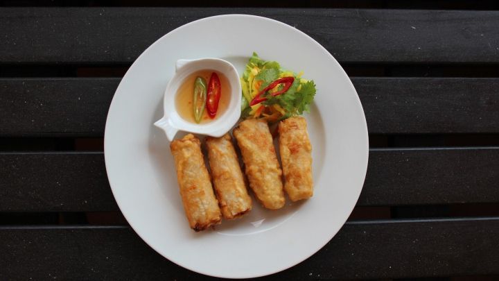 Frittierte Chilischoten liegen auf einem wei&szlig;en Teller, begleitet von einer Dipsauce und frischem Salat, auf einem dunklen Tisch.