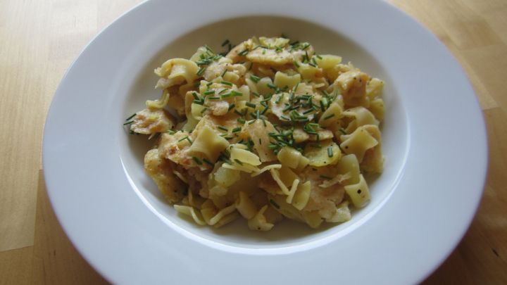 Ein Teller mit hausgemachter Pasta, garniert mit Kr&auml;utern, steht auf einem Holztablett neben einer Glaskaraffe.