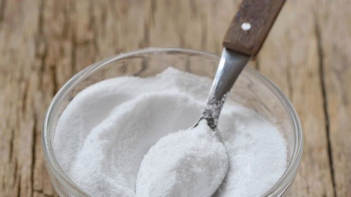 Ein Glas mit Natron und einem L&ouml;ffel steht auf einer Holzoberfl&auml;che, bereit f&uuml;r ein Peeling.