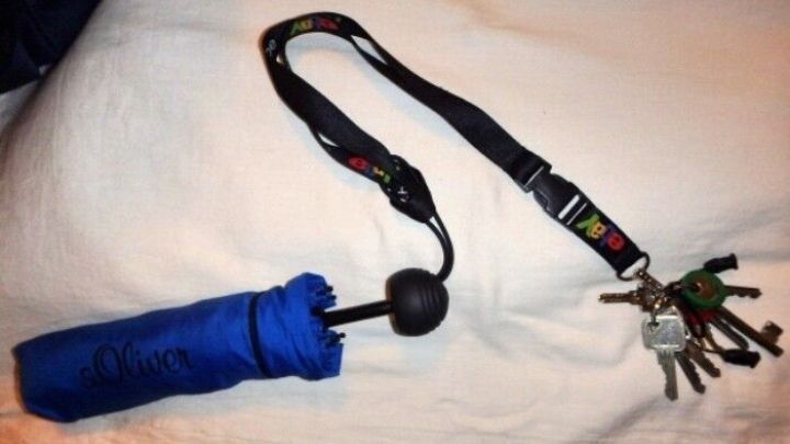 Ein blauer Regenschirm ist zusammengeklappt und liegt neben einem Schl&uuml;sselanh&auml;nger mit mehreren Schl&uuml;sseln auf einer wei&szlig;en Oberfl&auml;che.