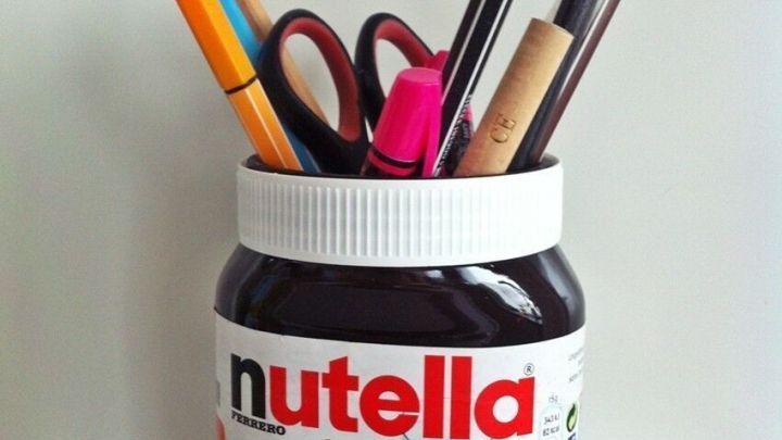 Ein Nutella-Glas dient als origineller Stifthalter, gef&uuml;llt mit verschiedenen Stiften und Scheren auf einem Tisch.