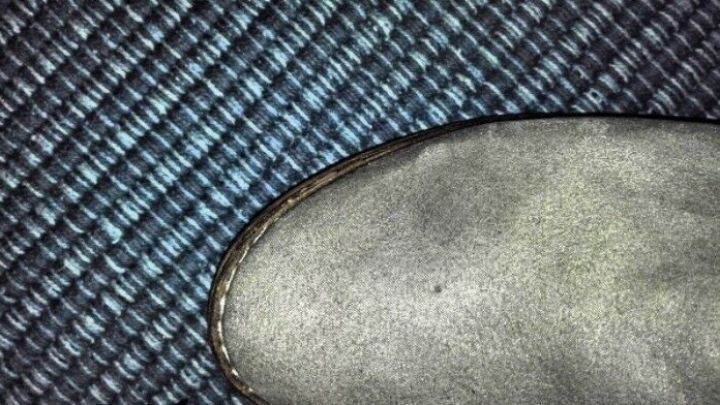 Ein Schuh aus Kunstwildleder liegt auf einem strukturierten Teppich, mit einem klebrigen Fleck auf der Oberfl&auml;che.