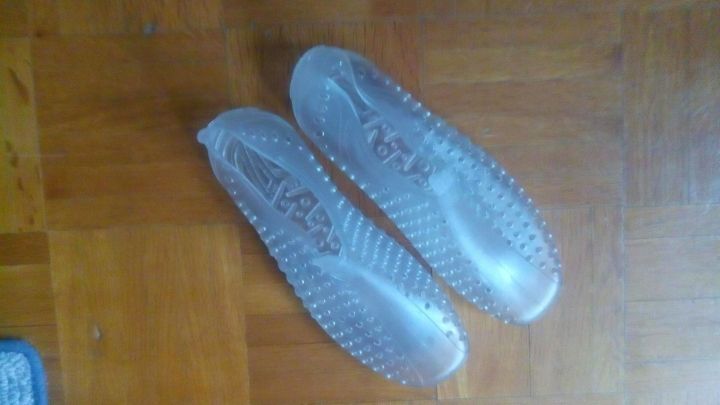 Transparente Anti-Rutsch-Schuhe liegen auf einem Holzboden, bereit f&uuml;r die Nutzung im Bad oder in der Dusche.