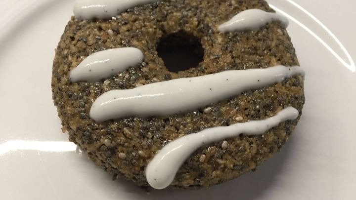 Ein Chia-Donut mit einer gl&auml;nzenden, wei&szlig;en Zitronen-Kokos-Creme-Dekoration liegt auf einem wei&szlig;en Teller.